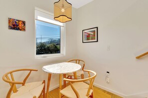 Una habitación con una mesa redonda, dos sillas de madera, un ventanal con vistas a la vegetación y dos cuadros enmarcados en la pared.