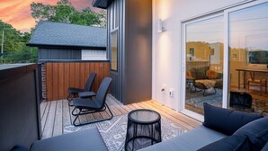 Een modern terras buiten met rieten meubilair, een glazen deur naar een binnenruimte en uitzicht op een zonsondergang.