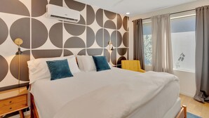 Een moderne slaapkamer met een bed, een plafondventilator, een airconditioning en een bedlampje, met uitzicht op het groen buiten door een raam.