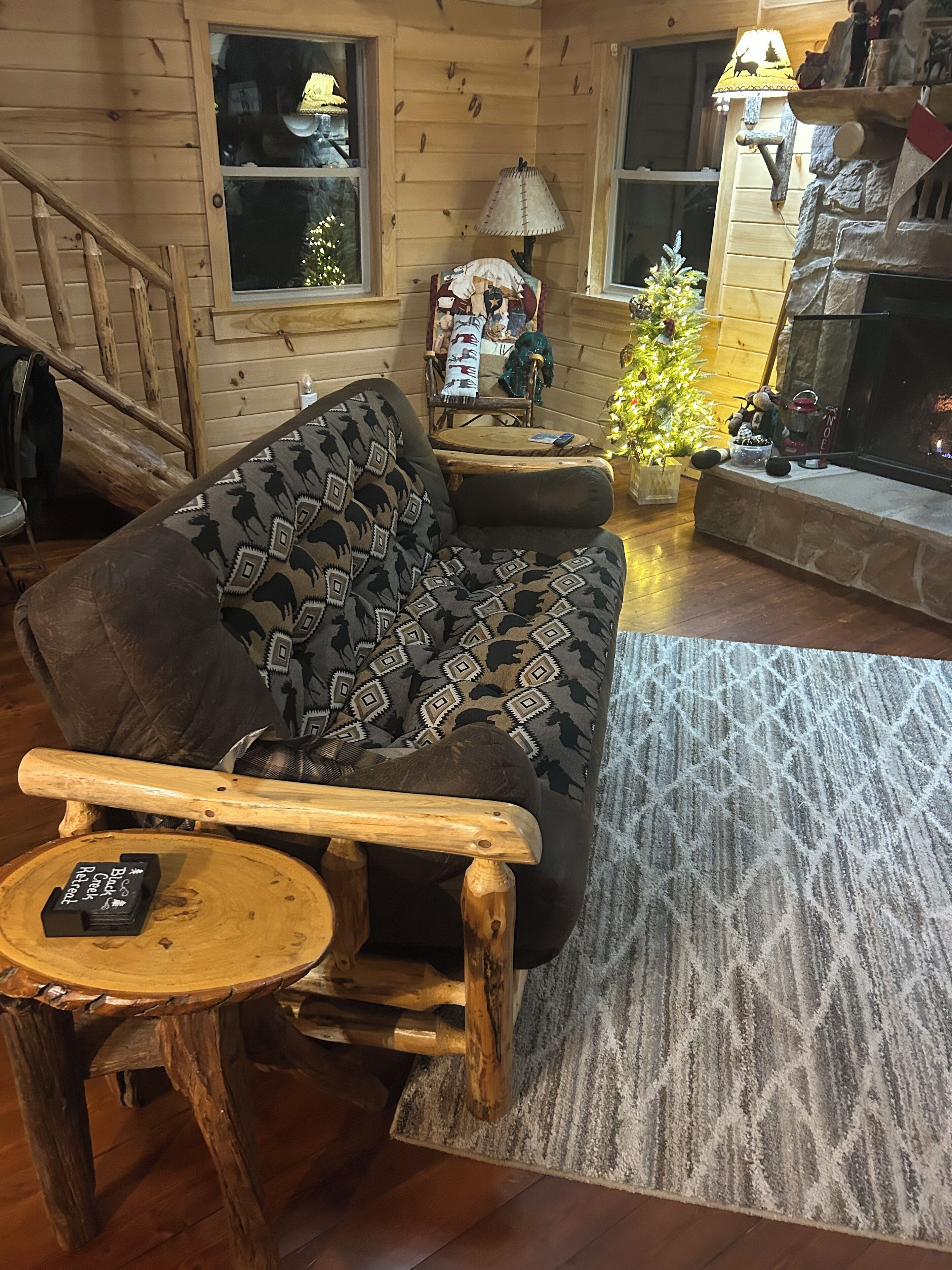 A cozy cabin interior with a wooden couch, a small wooden table, a Christmas tree, and a fireplace.