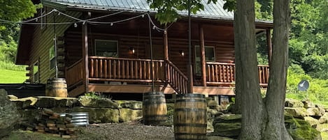 Ein rustikales Blockhaus mit Veranda, umgeben von Bäumen und einer Steinmauer.