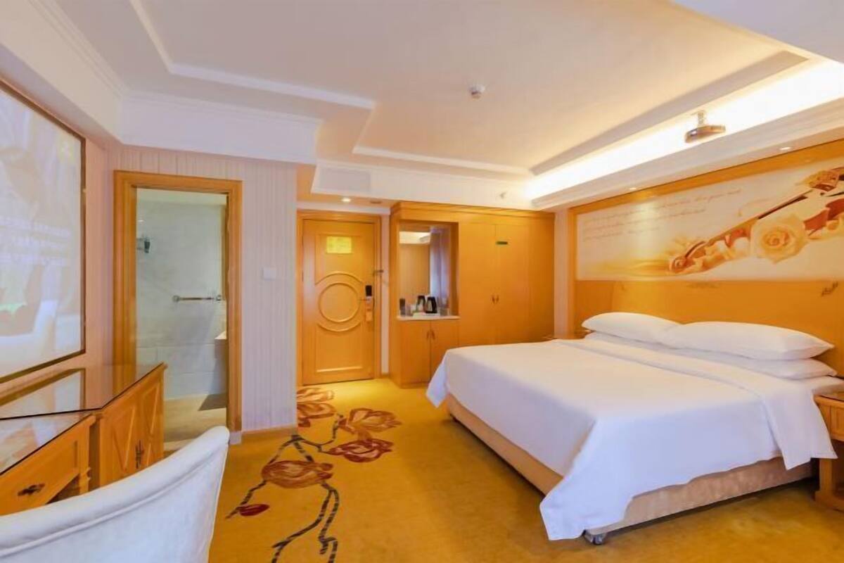 A hotel room with a bed, a mirror, a door, and a wall with a floral design.