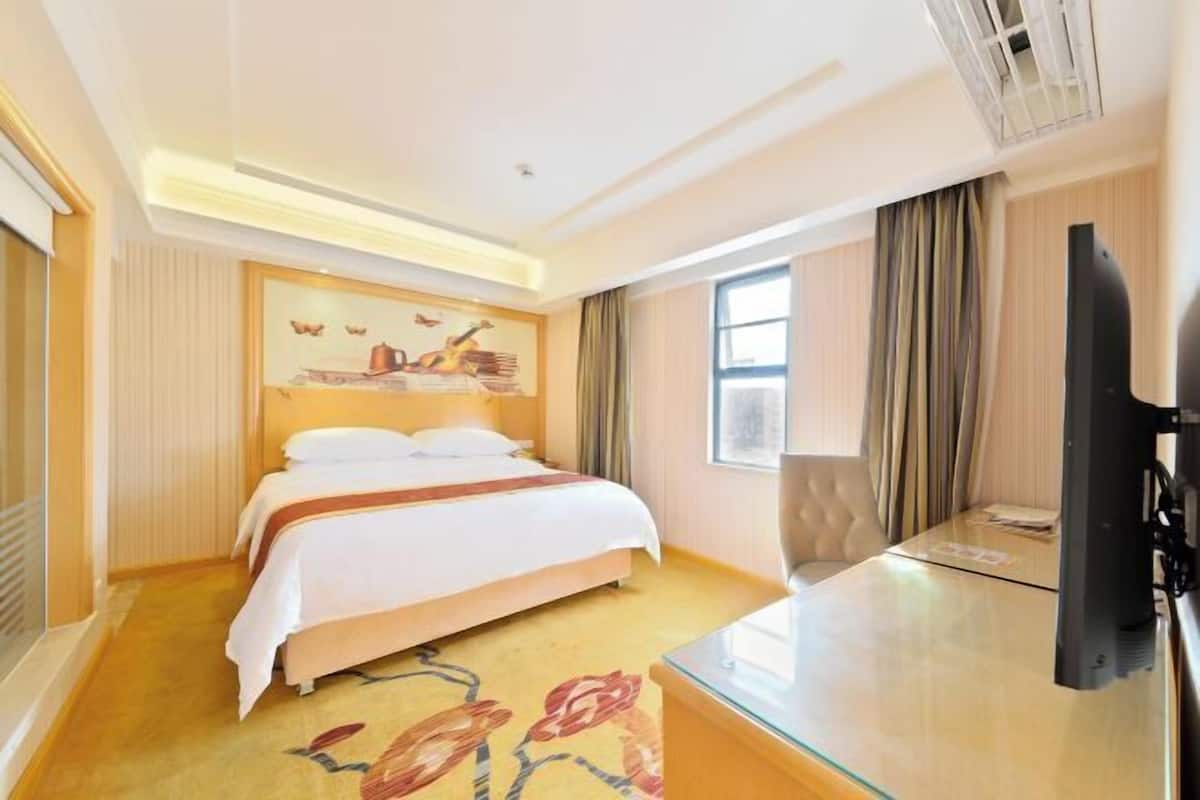 A hotel room with a bed, a desk, a television, and a window with curtains.