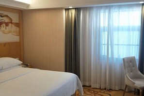 A hotel room with a bed, a chair, a painting on the wall, and a window with curtains. - Vienna Hotel (Shenzhen Gushu Metro Station) (Shenzhen)