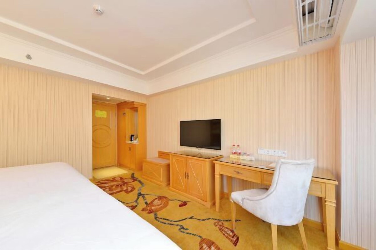 A hotel room with a bed, a desk with a chair, a television, and a wardrobe.