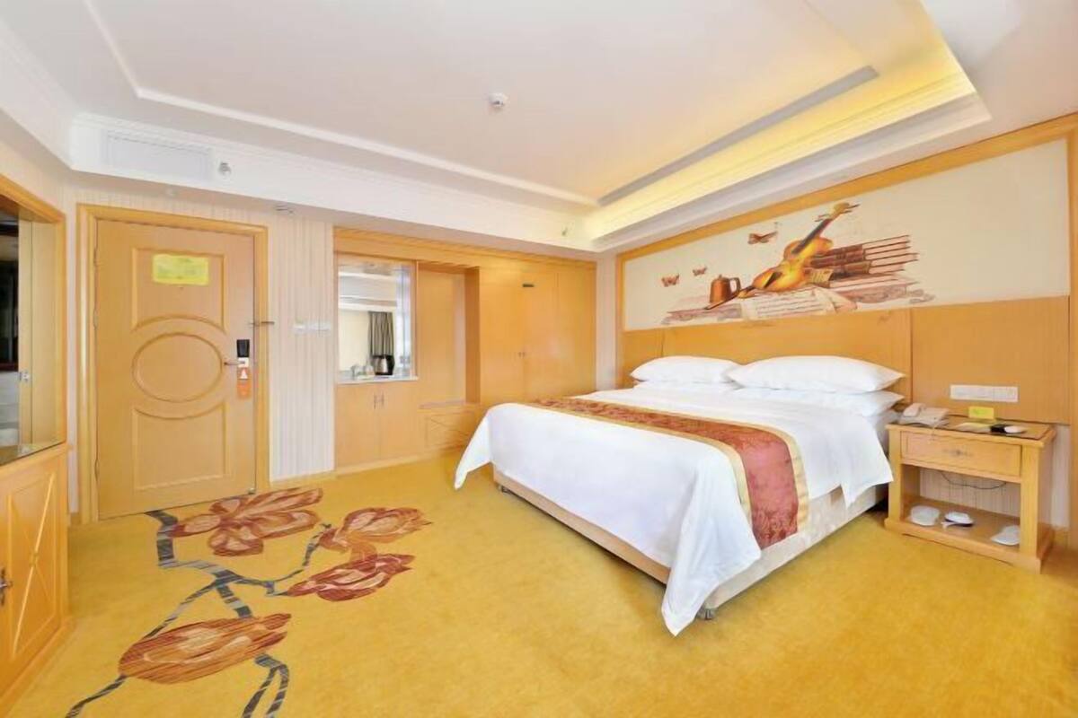 A hotel room with a bed, a nightstand, a desk, a mirror, and a floral carpet.