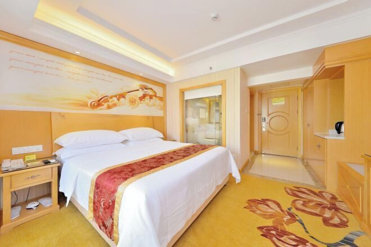 A hotel room with a bed, bedside table, and a large window.
