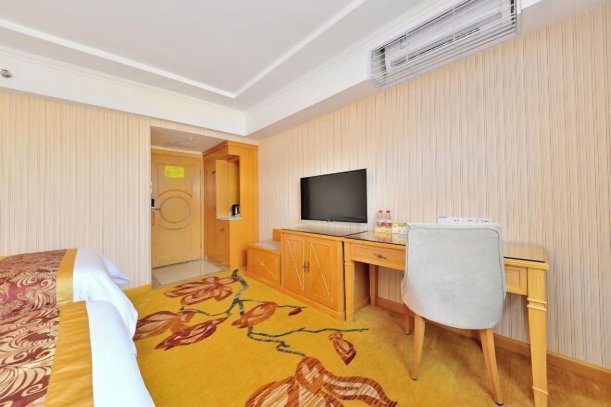 A hotel room with a bed, a desk, a chair, a television, and an air conditioning unit.