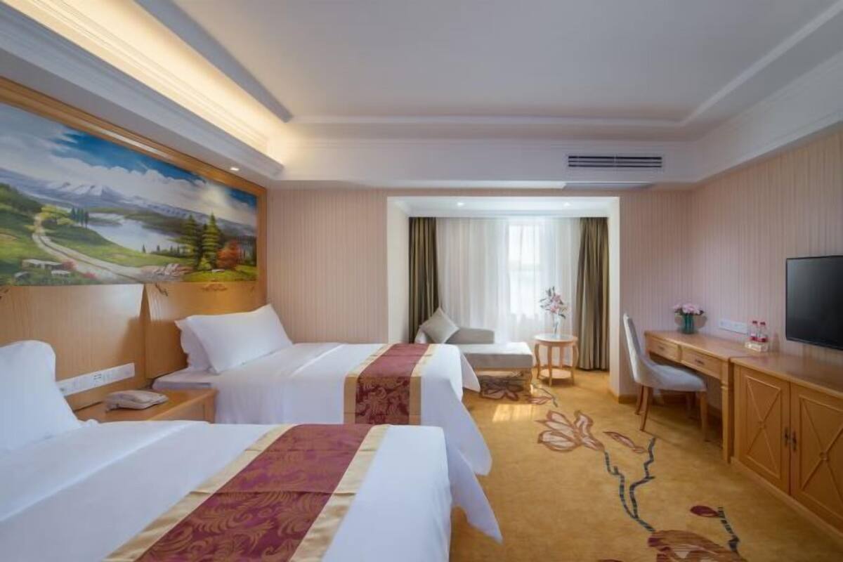 A hotel room with two beds, a desk, a TV, and a painting on the wall.