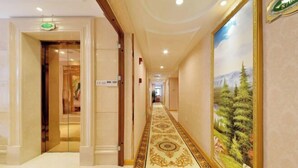 A hotel hallway with a patterned carpet, a painting of a forest, and a sign indicating the price of $70. - Vienna Hotel (Shenzhen Gushu Metro Station) (Shenzhen)
