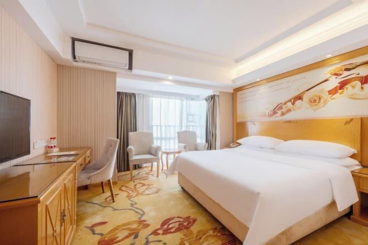 A hotel room with a bed, a desk, a TV, and a small table.