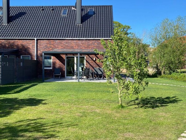 A modern house with a brick exterior, a covered patio with outdoor furniture, and a well-maintained lawn. - Holiday Home Ankerherz (Butjadingen)