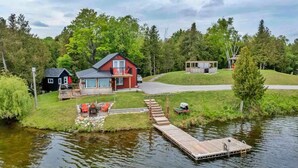 A lakeside property with a red house, a dock, and a small wooden structure. - Beautiful Private Lake Retreat - One of a kind! (Kawartha Lakes)