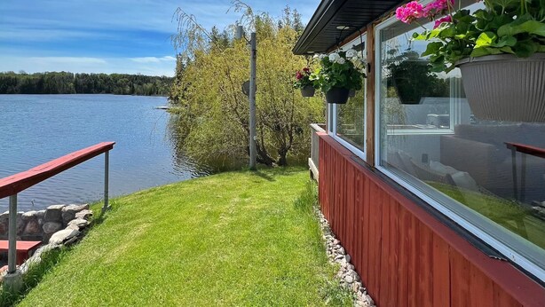 A lakeside view with a wooden deck, a red railing, and a window overlooking the water. - Beautiful Private Lake Retreat - One of a kind! (Kawartha Lakes)
