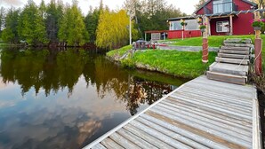 A wooden dock leading to a house with a red exterior, a small garden, and a calm lake. - Beautiful Private Lake Retreat - One of a kind! (Kawartha Lakes)