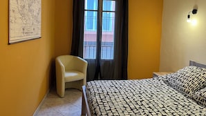 A room with a bed, a chair, a map on the wall, and a window with curtains. - Appartement Proche de la Mer, Idéal Pour 2 à 4 Personnes, Garage Privé (Collioure)