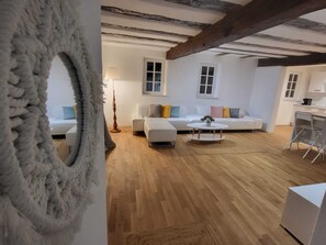 A modern living room with a white sofa, a coffee table, and a lamp. There is a wooden floor and a ceiling with exposed beams. - Pension Kostera 35,00 Pro Person Ökologisch ,platz bis zu 12 Personen (Babenhausen)