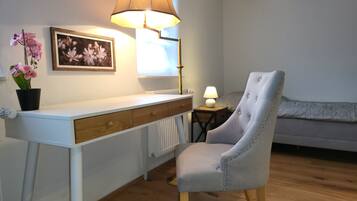 Een slaapkamer met een bed, een bureau met lamp, een stoel, een radiator en een potorkidee.