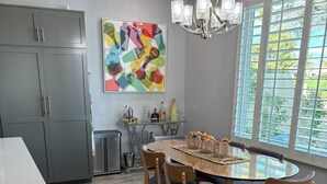 Een moderne keuken met grijze kastjes, een eettafel met stoelen, een kroonluchter en een groot raam met uitzicht.