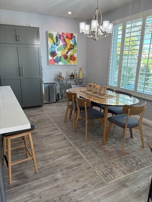 Une cuisine moderne avec des meubles gris, une table à manger avec des chaises, un lustre et une grande fenêtre donnant sur un beau paysage.