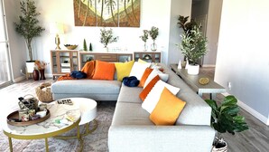 Een moderne woonkamer met een grijze modulaire bank, een ronde salontafel en een groot schilderij van palmbomen.