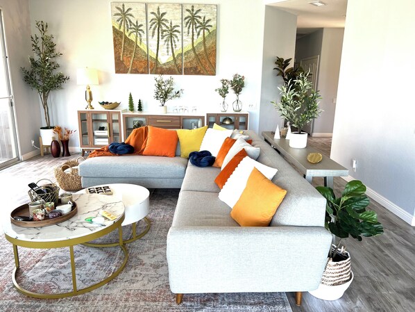 Een moderne woonkamer met een grijze modulaire bank, een ronde salontafel en een groot schilderij van palmbomen aan de muur.