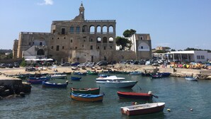 Un bâtiment historique doté d’arcs en plein cintre et surmonté d’un clocher, entouré d’un port de plaisance où sont amarrés différents types de bateaux.