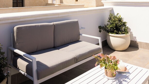 Une terrasse sur le toit avec un canapé blanc, une table blanche et des plantes en pot.
