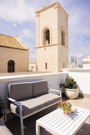 Terraza en la azotea con un sofá blanco, una mesa blanca y plantas en macetas.