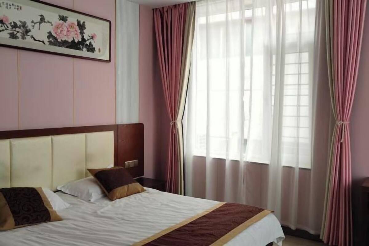 A hotel room with a bed, a headboard, a painting, and curtains.