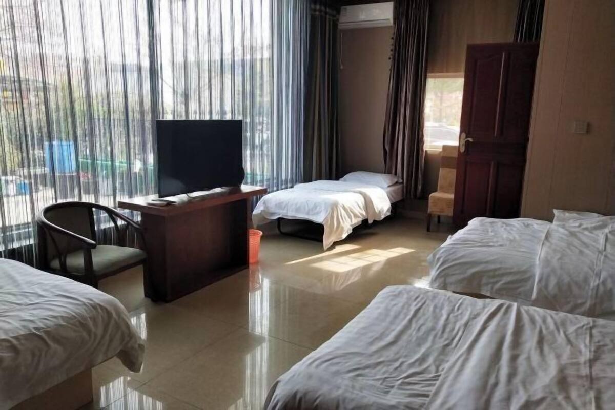 A hotel room with a bed, a desk with a television, a chair, and a view through sheer curtains.