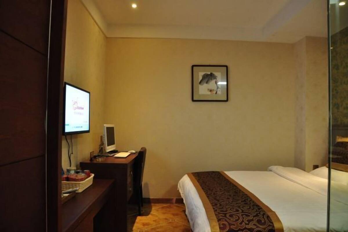 A hotel room with a bed, a desk with a computer, a television, and a framed picture on the wall.