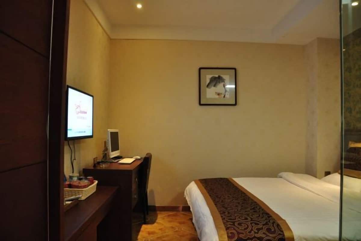 A hotel room with a bed, a desk with a computer, a television, and a framed picture on the wall.