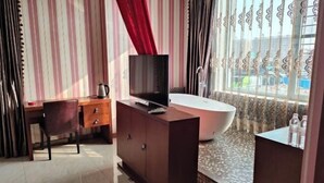 A modern bathroom with a bathtub, a vanity with a mirror, and a television on a cabinet. - Donggang Xinxiangyuan Hotel (Donggang)