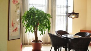 A dining area with a round table and wicker chairs, a potted plant, and a framed artwork on the wall. - Donggang Xinxiangyuan Hotel (Donggang)
