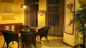 A room with a round table and four chairs, a bench, a wall-mounted air conditioner, a framed picture, and a potted plant. - Donggang Xinxiangyuan Hotel (Donggang)