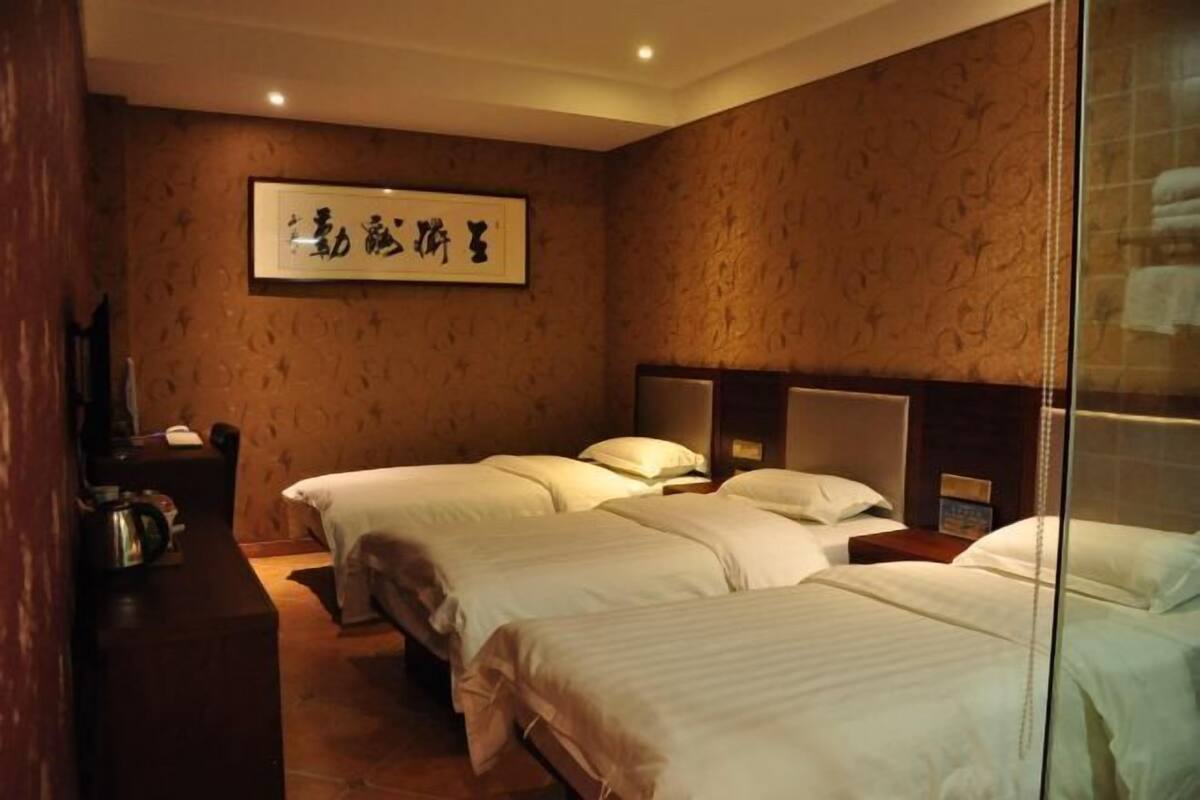 A hotel room with two beds, a wooden headboard, a framed artwork on the wall, and a small table with a kettle.