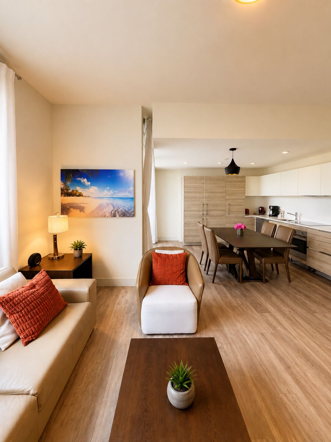 A modern living room with a sofa, a coffee table with a plant, a dining area with a table and chairs, and a kitchen with cabinets and appliances.