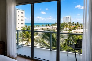 A balcony with a view of the ocean and palm trees, a chair, and a building in the background. - Global Rent Apart (Hollywood)