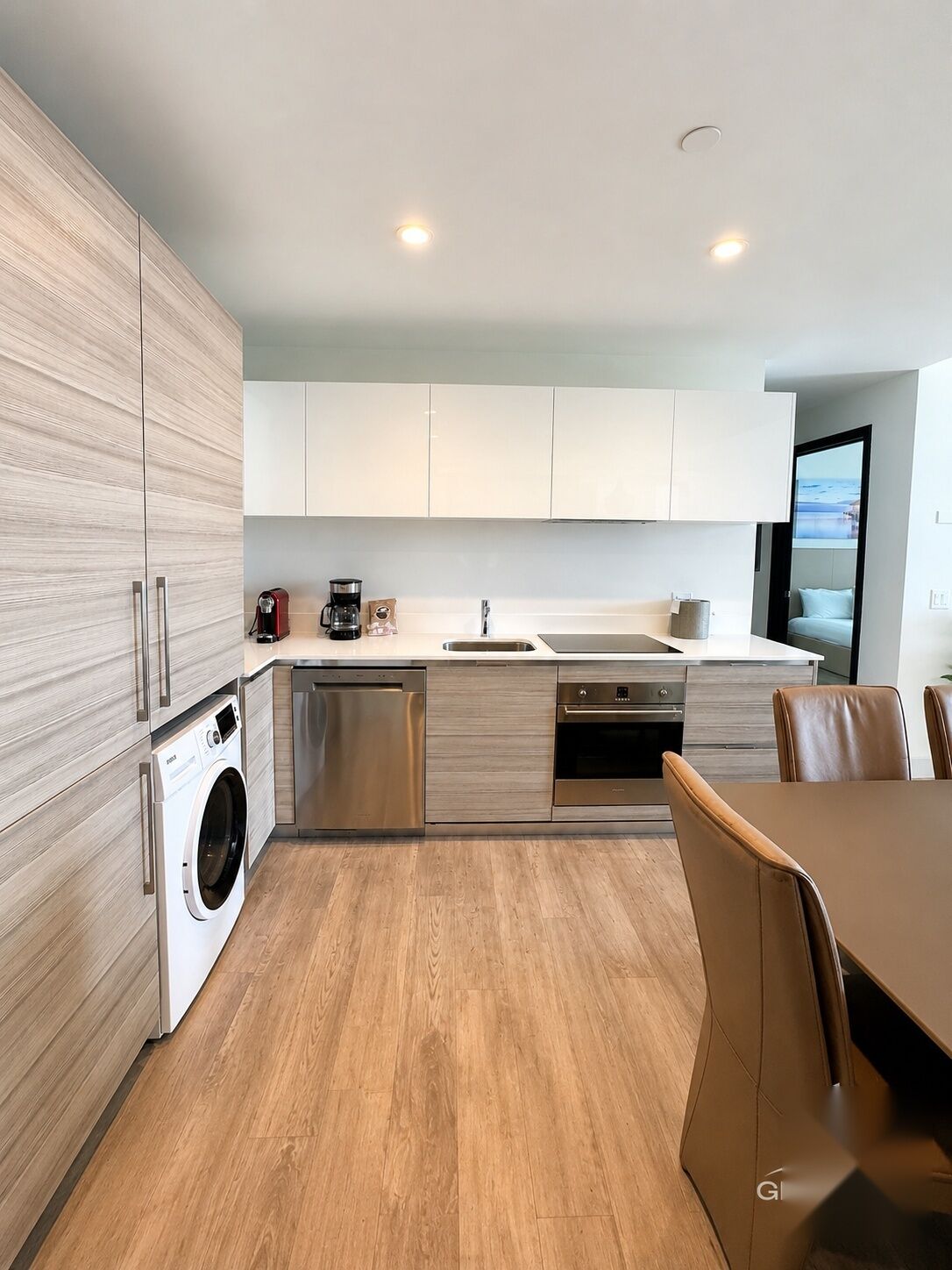 A modern kitchen with built-in appliances, a dining area with a table and chairs, and a view through a window.