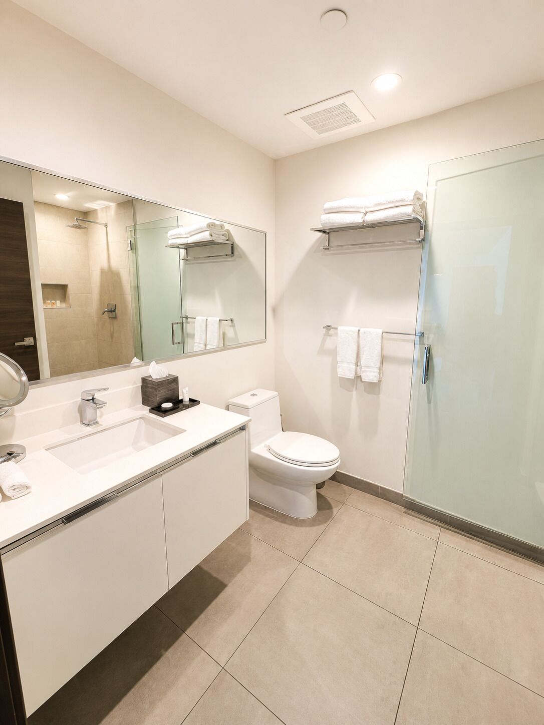 A modern bathroom with a glass shower enclosure, a white sink with a mirror, a toilet, and a towel rack.
