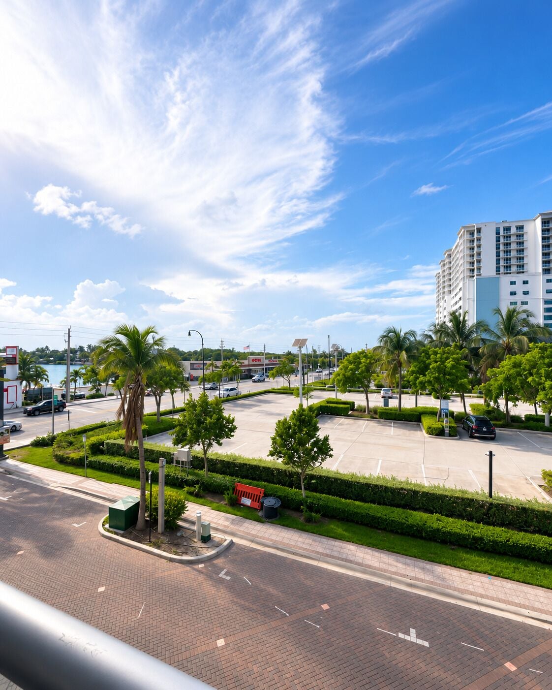 A parking area with palm trees and a road leading to a building.