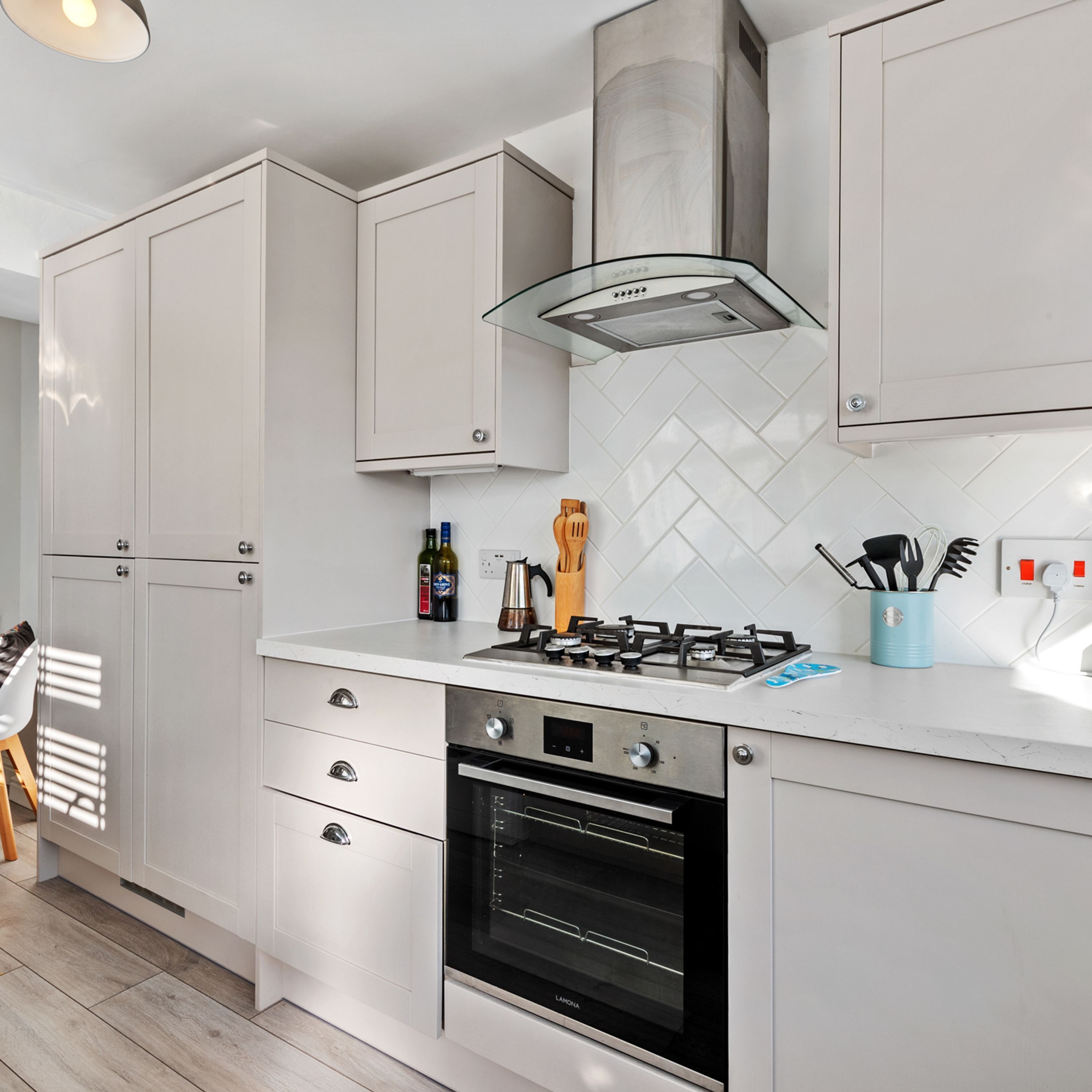 A modern kitchen with white cabinetry, a gas stove, an oven, and a glass range hood.