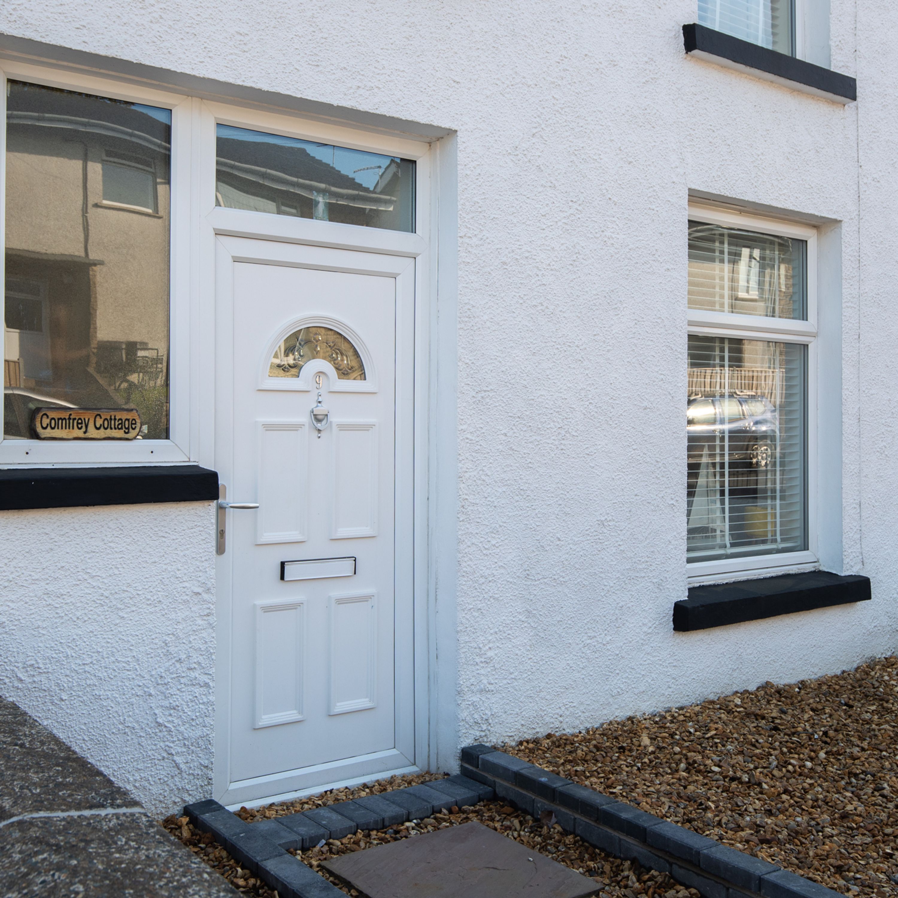 A white door with a small window above it, a mailbox, and a sign that reads "Comfrey Cottage."