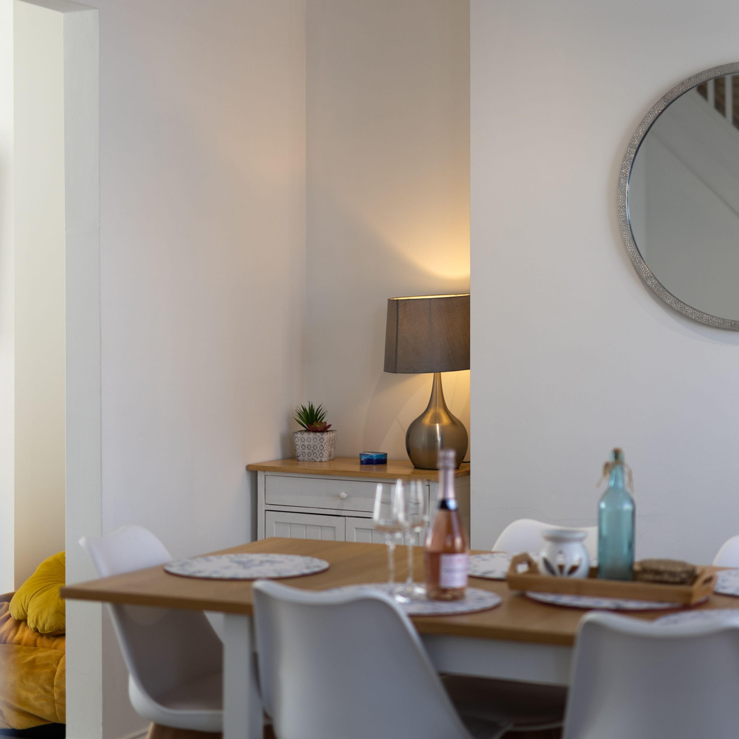 En matplats med ett bord dukat för fyra personer, en lampa, en krukväxt och en flaska på bordet.