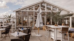 An outdoor café with tables and chairs, a large umbrella, and a view of the sea. - Beach House in Wijk aan Zee With Sea Views (Wijk aan Zee)