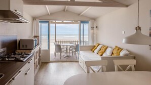 A compact kitchen with a view to the beach, a dining area with a white table and chairs, and a cozy seating area with cushions. - Beach House in Wijk aan Zee With Sea Views (Wijk aan Zee)
