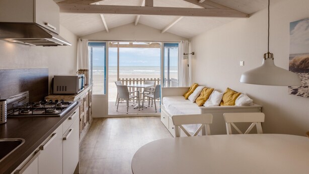 A kitchen with a stove, microwave, and cabinets, leading to a balcony with a view of the beach. - Beach House in Wijk aan Zee With Sea Views (Wijk aan Zee)