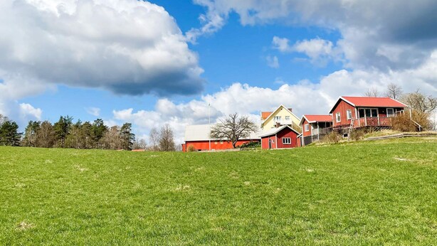 A rural landscape with a red barn and a yellow house on a grassy hill under a partly cloudy sky. - 5 Person Holiday Home in Bredared (Bredared)