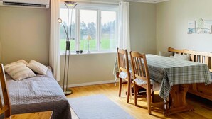 A room with a bed, a table with chairs, a window with a view of greenery, and an air conditioning unit. - 5 Person Holiday Home in Bredared (Bredared)